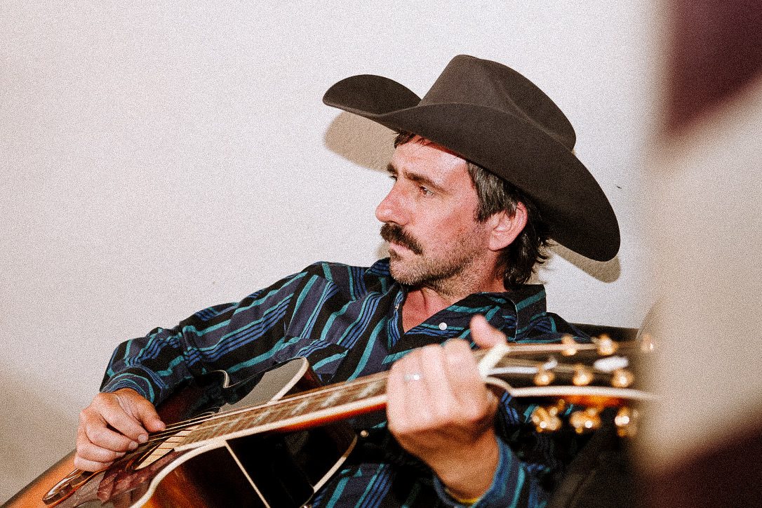 Dave Kent in a cowboy hat playing acoustic guitar